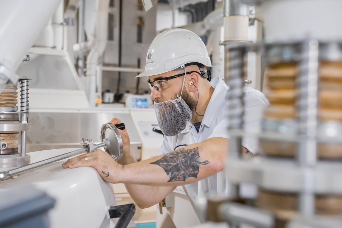Man making adjustments on milling equipment wearing safety gear in the Busch Grains factory.